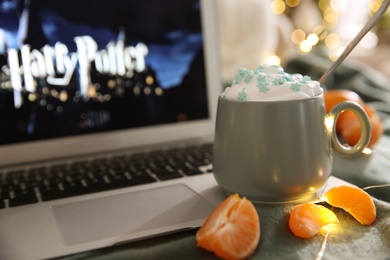 Photo of MYKOLAIV, UKRAINE - DECEMBER 25, 2020: Laptop displaying Harry Potter movie indoors, focus on cup of sweet drink and tangerine slices.  Cozy winter holidays atmosphere
