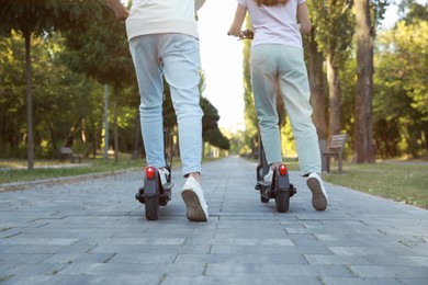 Photo of Couple riding modern electric kick scooters in park, back view