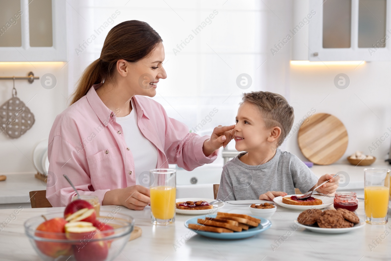 Photo of Mother and her cute little son having breakfast at table in kitchen