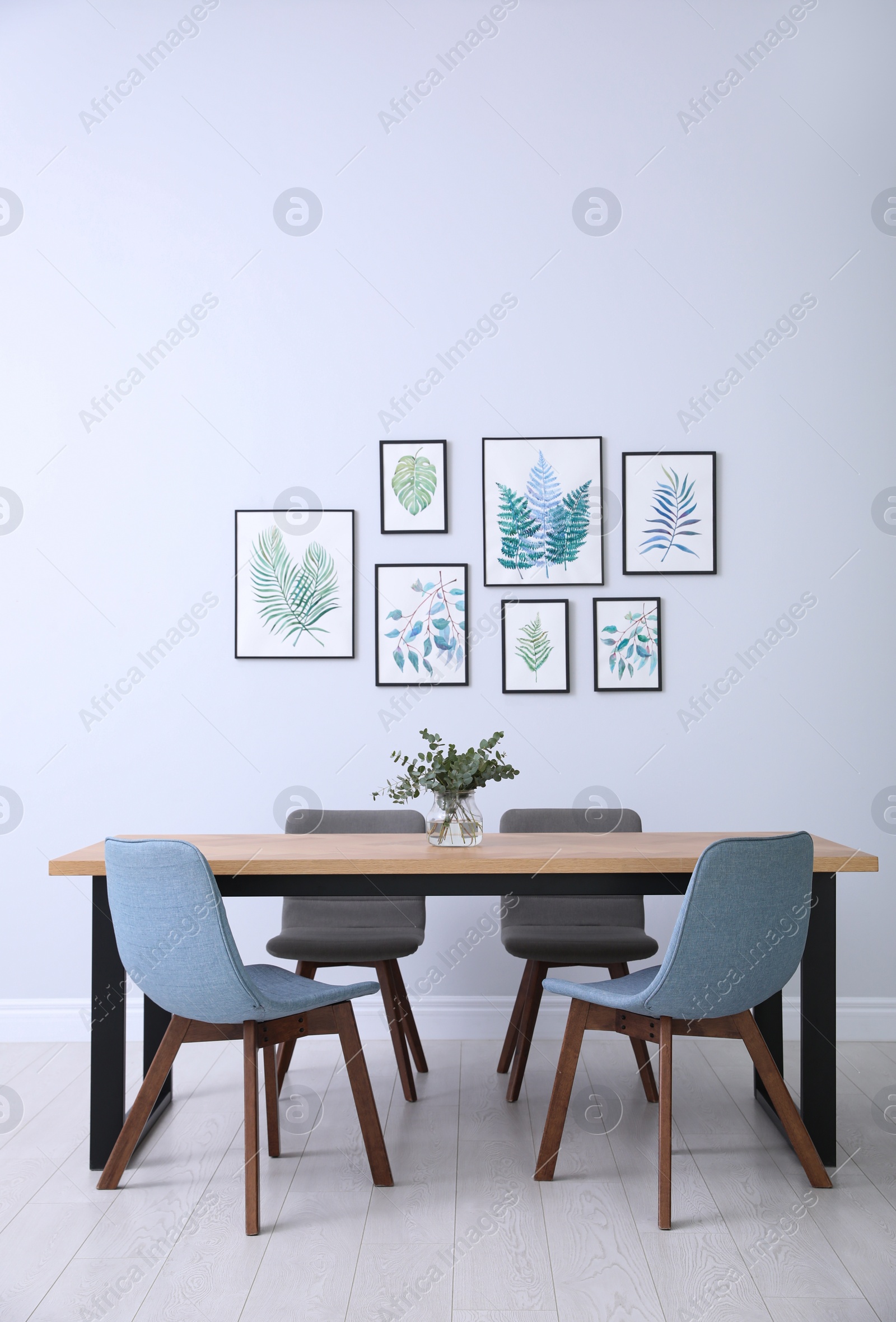 Photo of Stylish room interior with modern table, chairs and paintings of tropical leaves. Idea for design