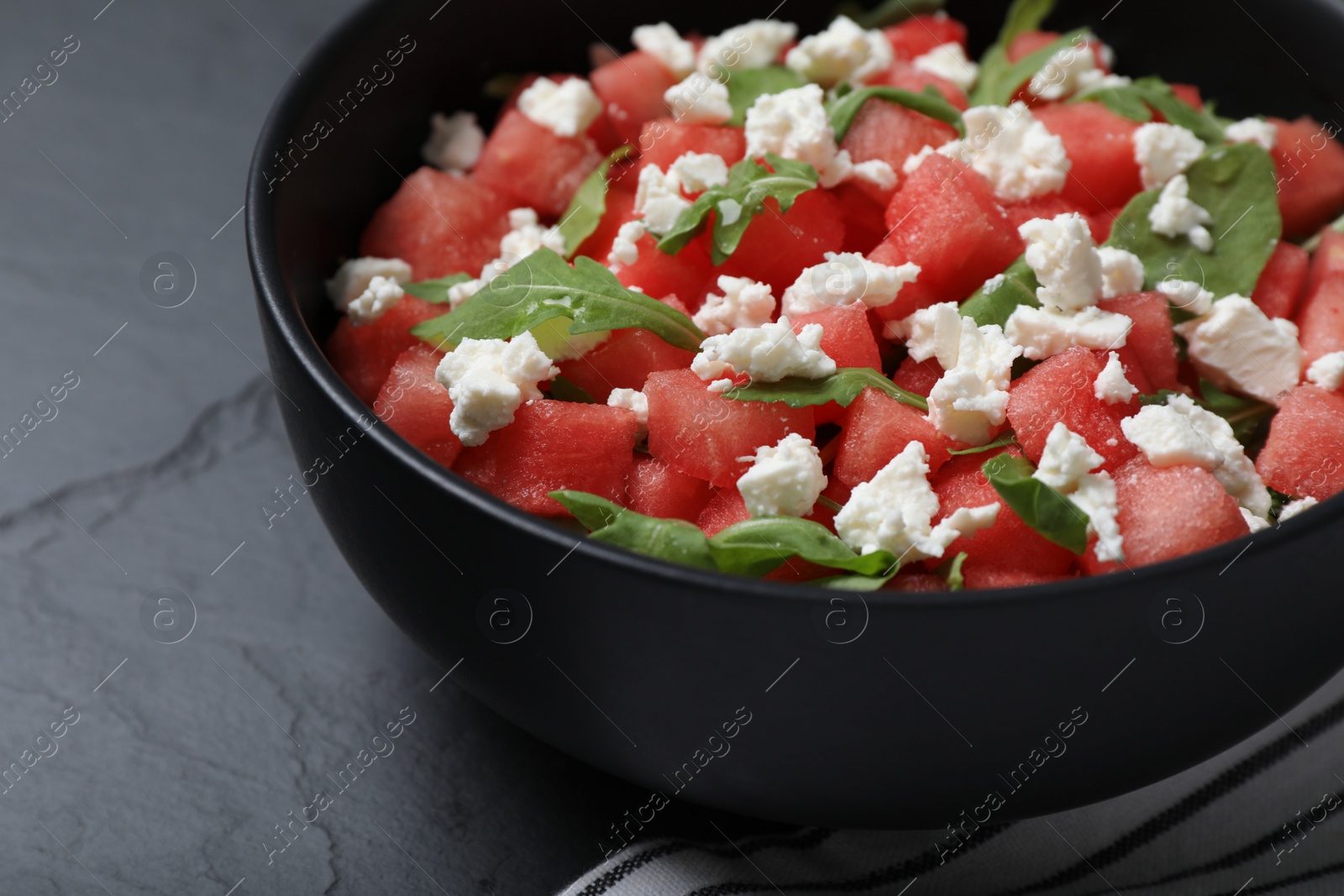 Photo of Delicious salad with watermelon, arugula and feta cheese on black table, closeup