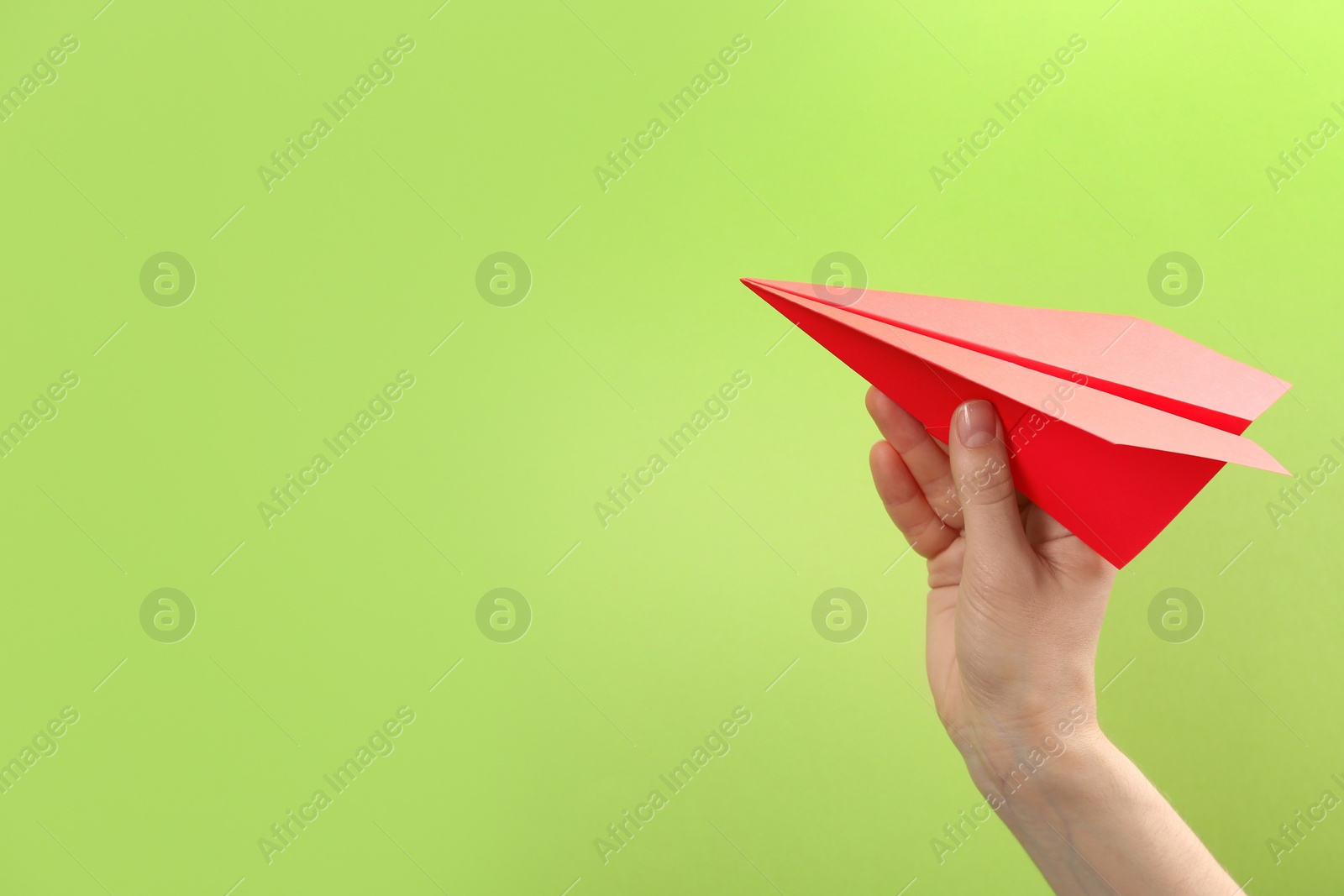 Photo of Woman holding paper plane on green background, closeup. Space for text