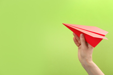 Woman holding paper plane on green background, closeup. Space for text