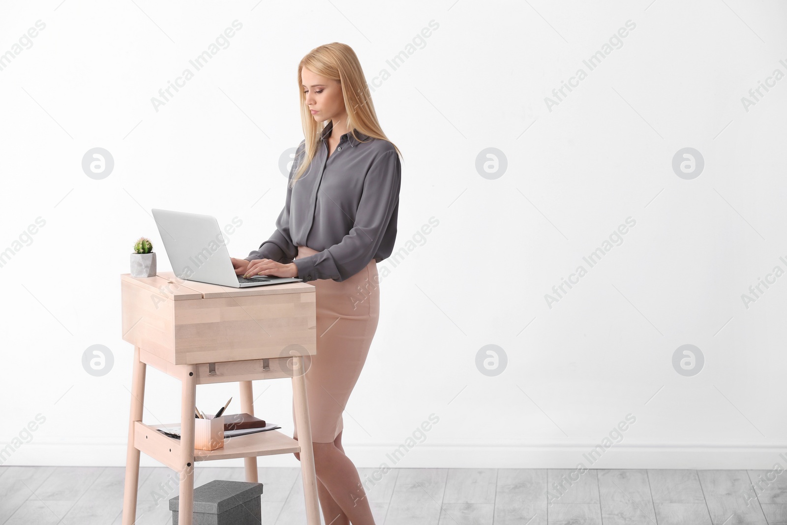 Photo of Young woman using laptop at stand up workplace against white wall. Space for text