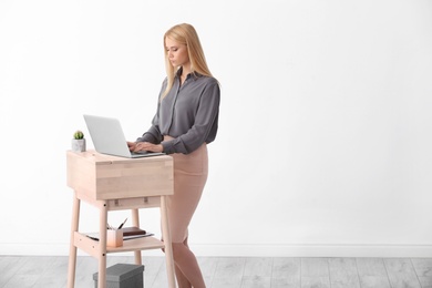 Young woman using laptop at stand up workplace against white wall. Space for text