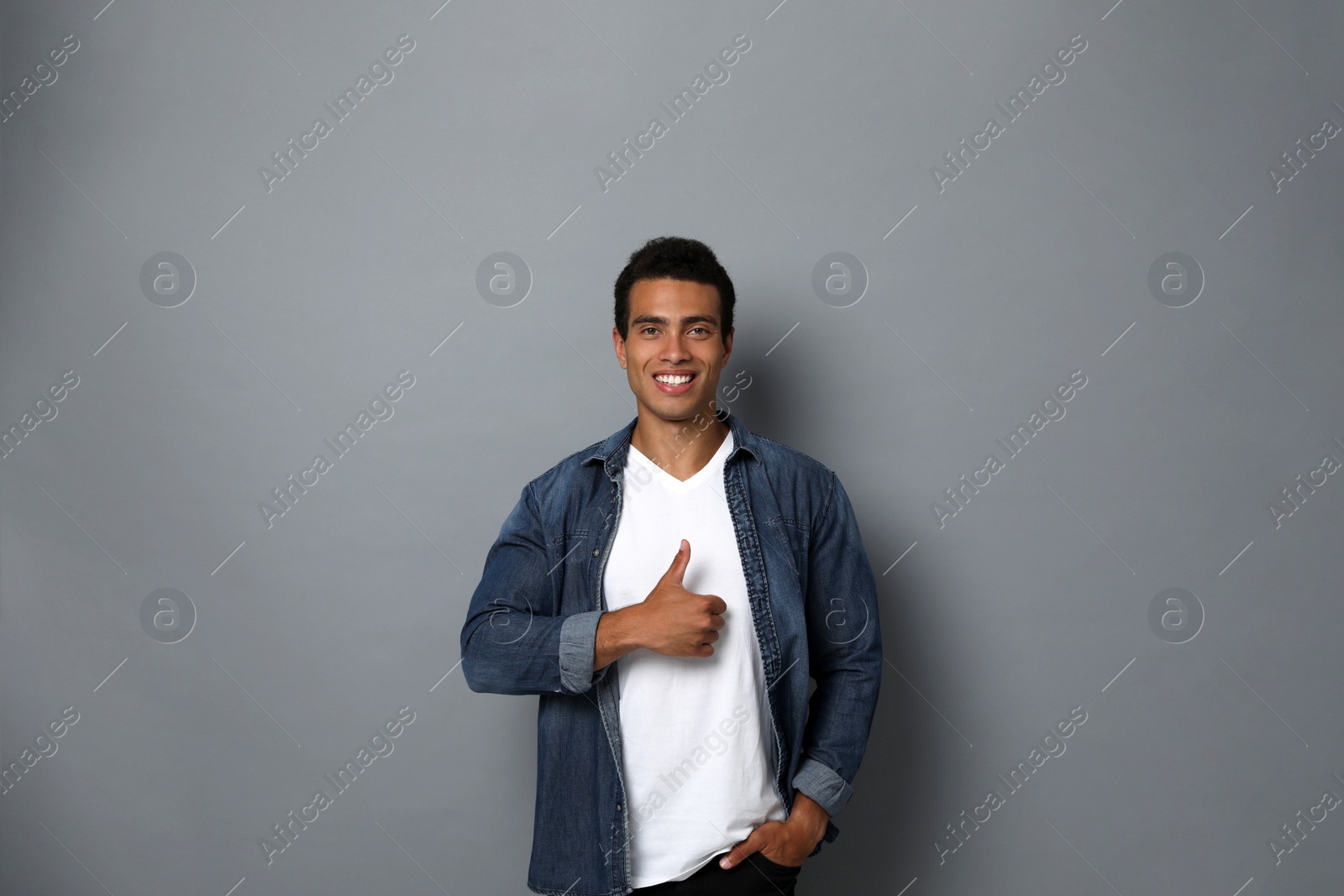 Photo of Handsome young African-American man showing thumbs-up gesture on grey background