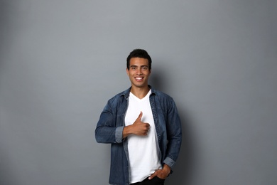 Handsome young African-American man showing thumbs-up gesture on grey background