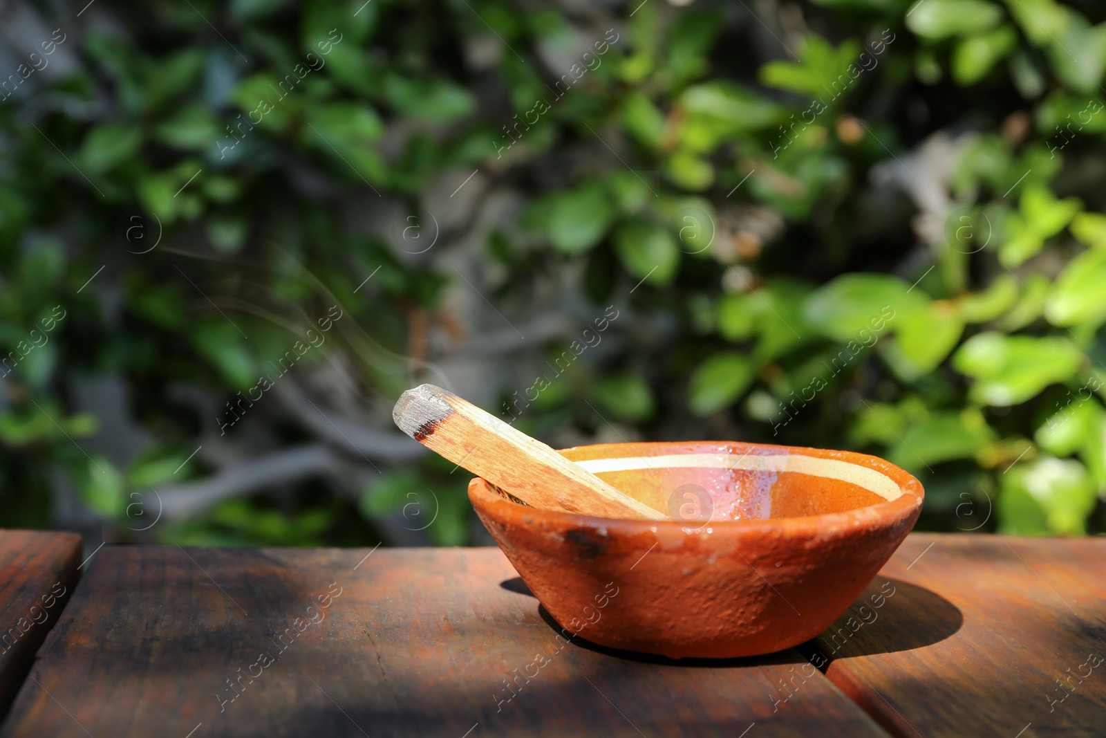 Photo of Palo santo stick in bowl on wooden table outdoors, space for text