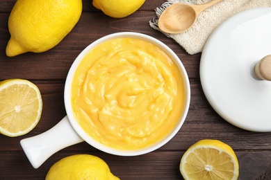 Delicious lemon curd in saucepan on dark wooden table, flat lay