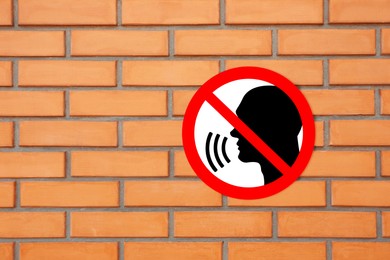 Illustration of Quiet Please prohibition sign with human head image on orange brick wall