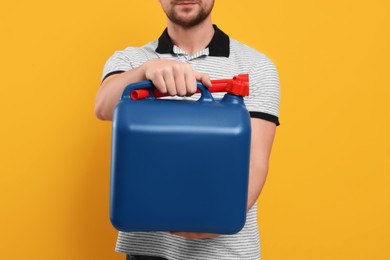 Photo of Man holding blue canister on orange background, closeup