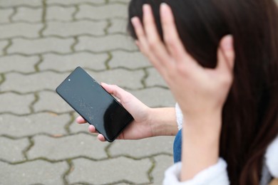 Woman holding damaged smartphone outdoors, closeup. Device repairing