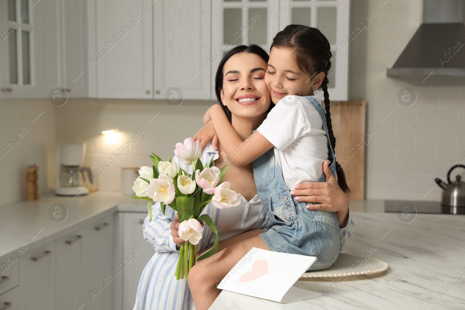 Photo of Little daughter congratulating her mom in kitchen at home. Happy Mother's Day