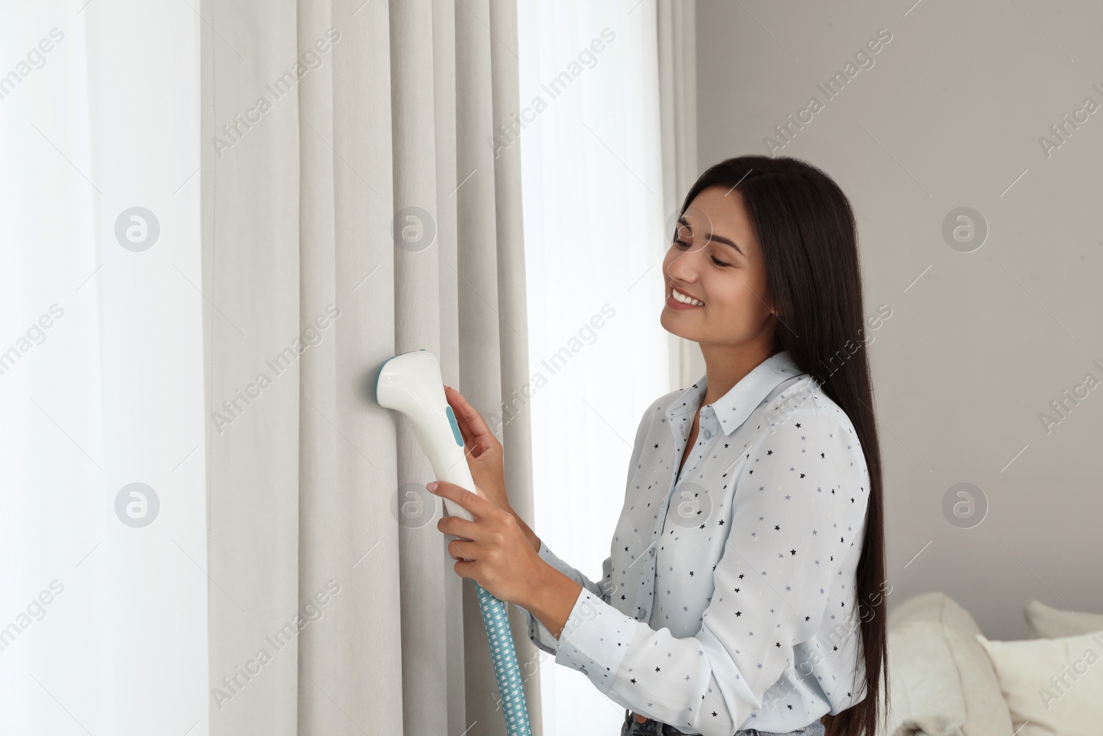 Photo of Woman steaming curtain near window at home. Space for text