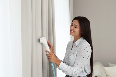 Woman steaming curtain near window at home. Space for text