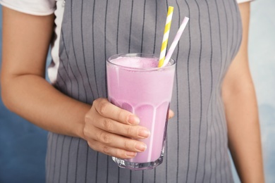 Woman with glass of delicious milk shake on color background, closeup