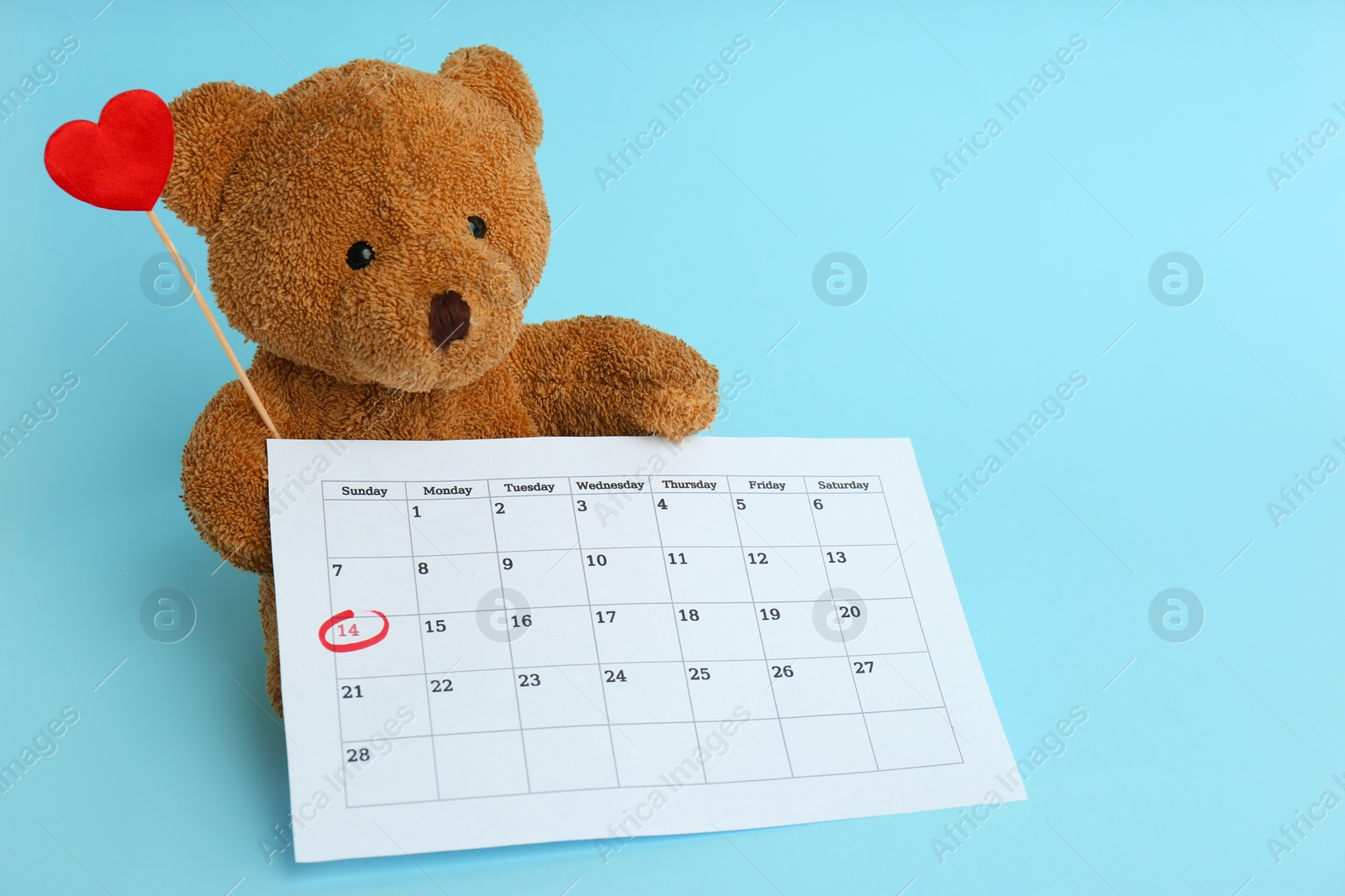 Photo of Cute teddy bear with calendar and red heart on light blue background. Valentine's day celebration