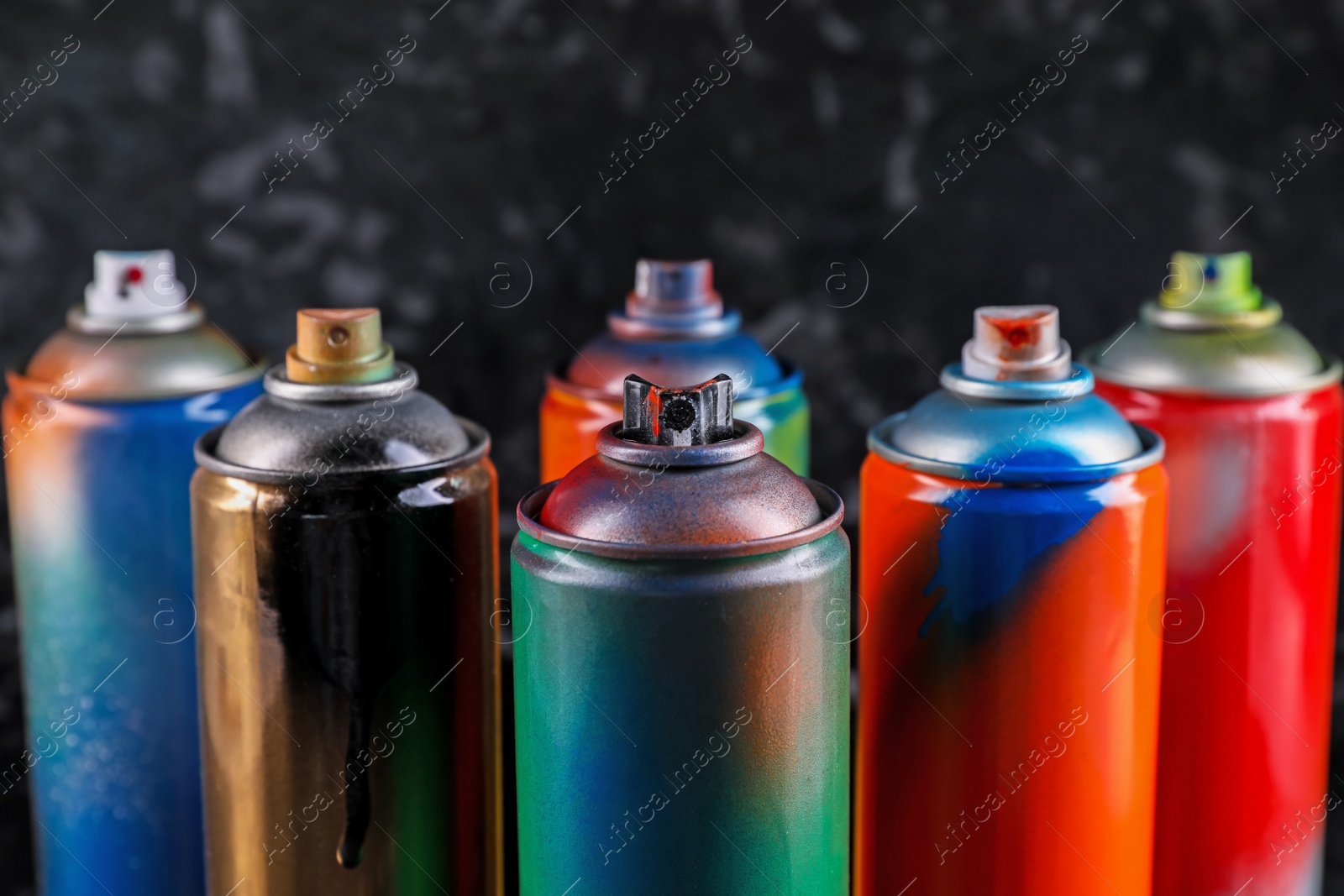 Photo of Used cans of spray paint on black marble background, closeup