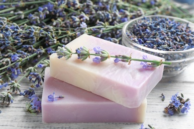 Photo of Handmade soap bars with lavender flowers on white wooden table, closeup