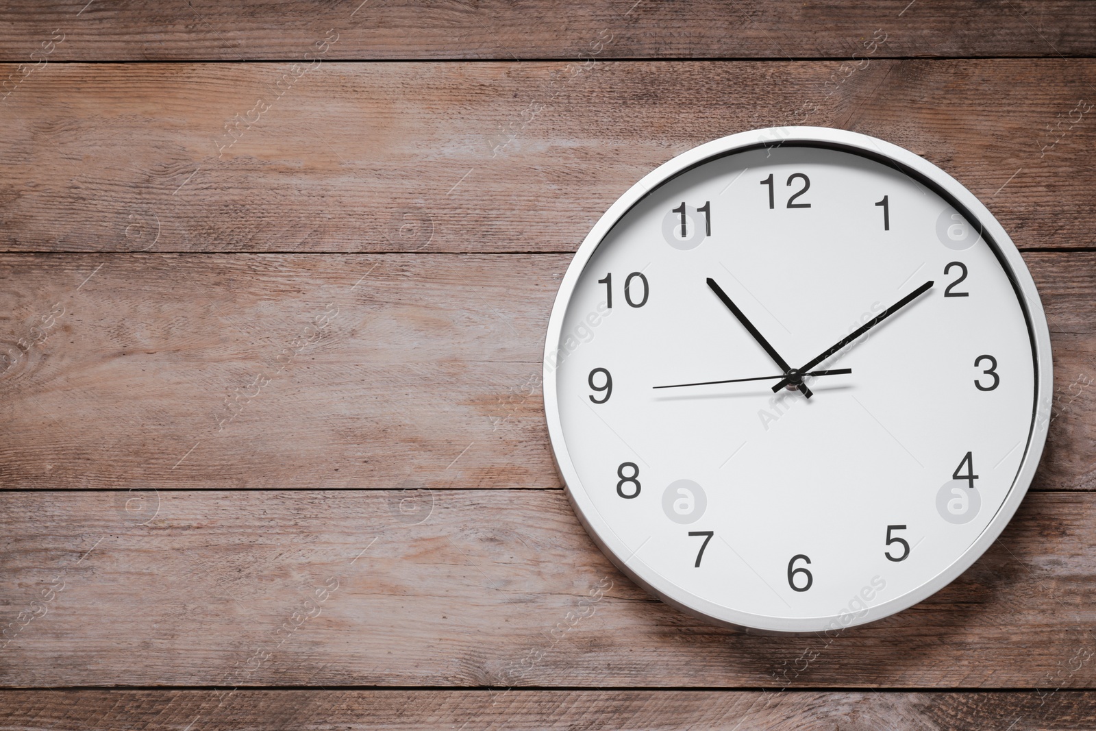 Photo of Stylish round clock on wooden table, top view with space for text. Interior element