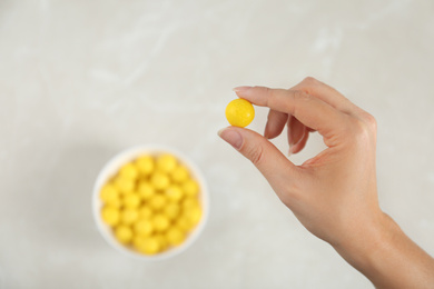 Photo of Woman holding tasty lemon drop above light table, top view