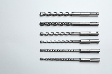 Different drill bits on light background, flat lay. Space for text