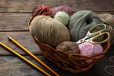 Photo of Soft woolen yarns, knitting needles and scissors on wooden table