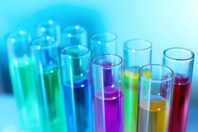 Photo of Many test tubes with colorful liquids on blurred background, closeup