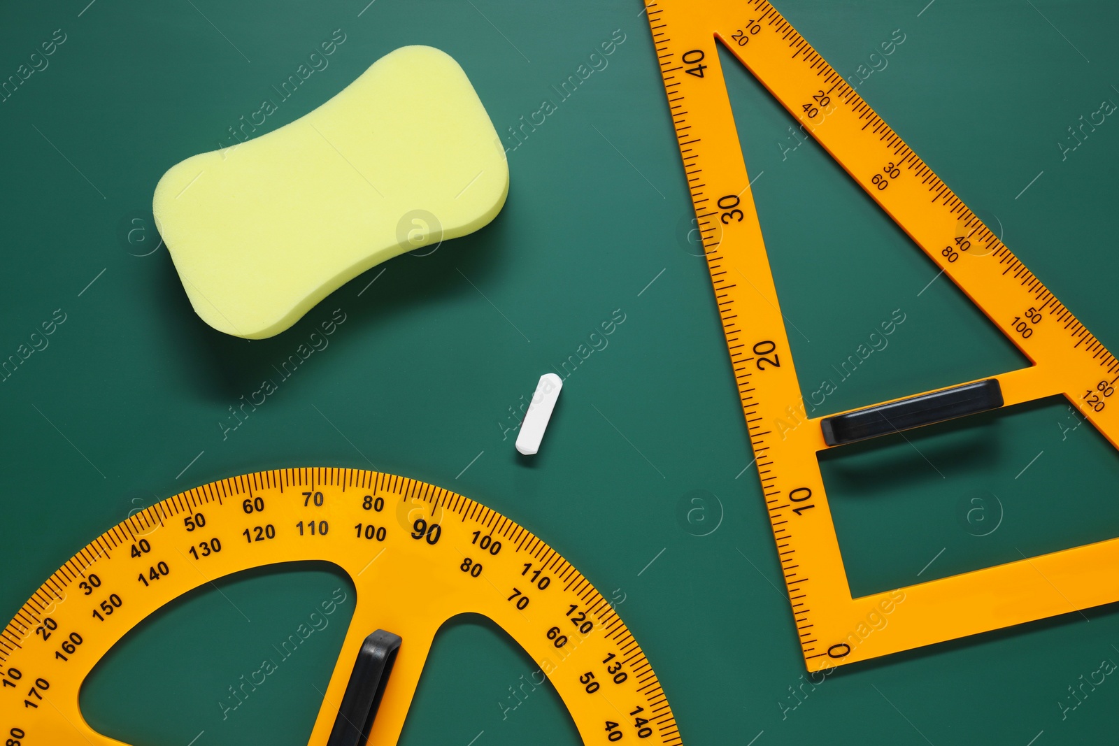 Photo of Protractor, triangle, sponge and chalk on green chalkboard, flat lay