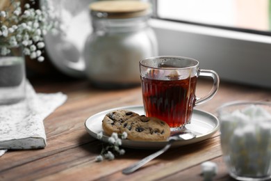 Photo of Cup of freshly brewed tea and delicious cookies on wooden table