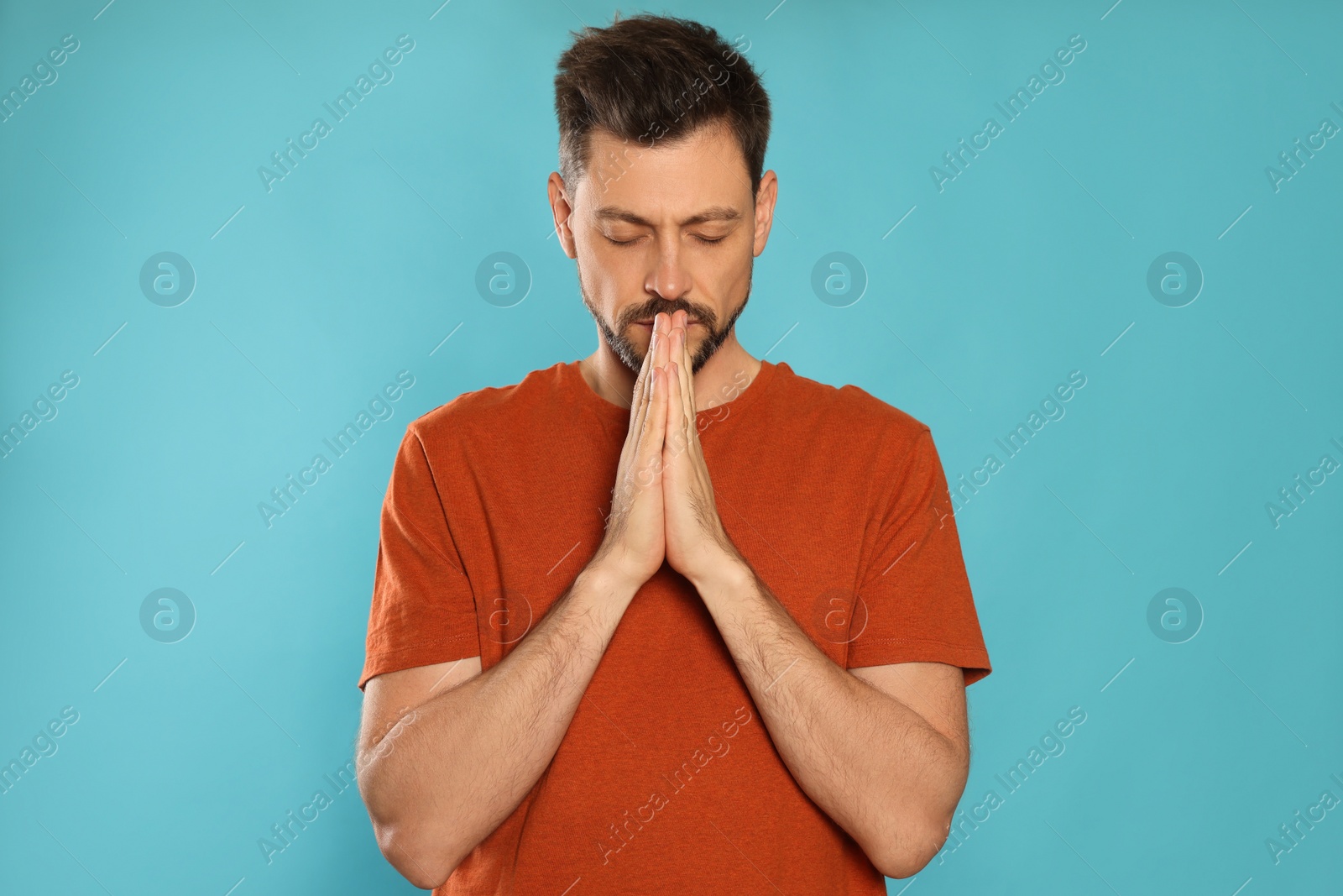 Photo of Man with clasped hands praying on turquoise background