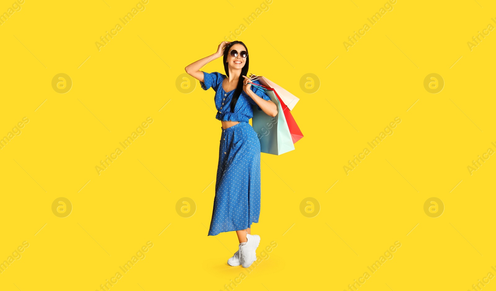 Photo of Beautiful young woman with paper shopping bags on yellow background