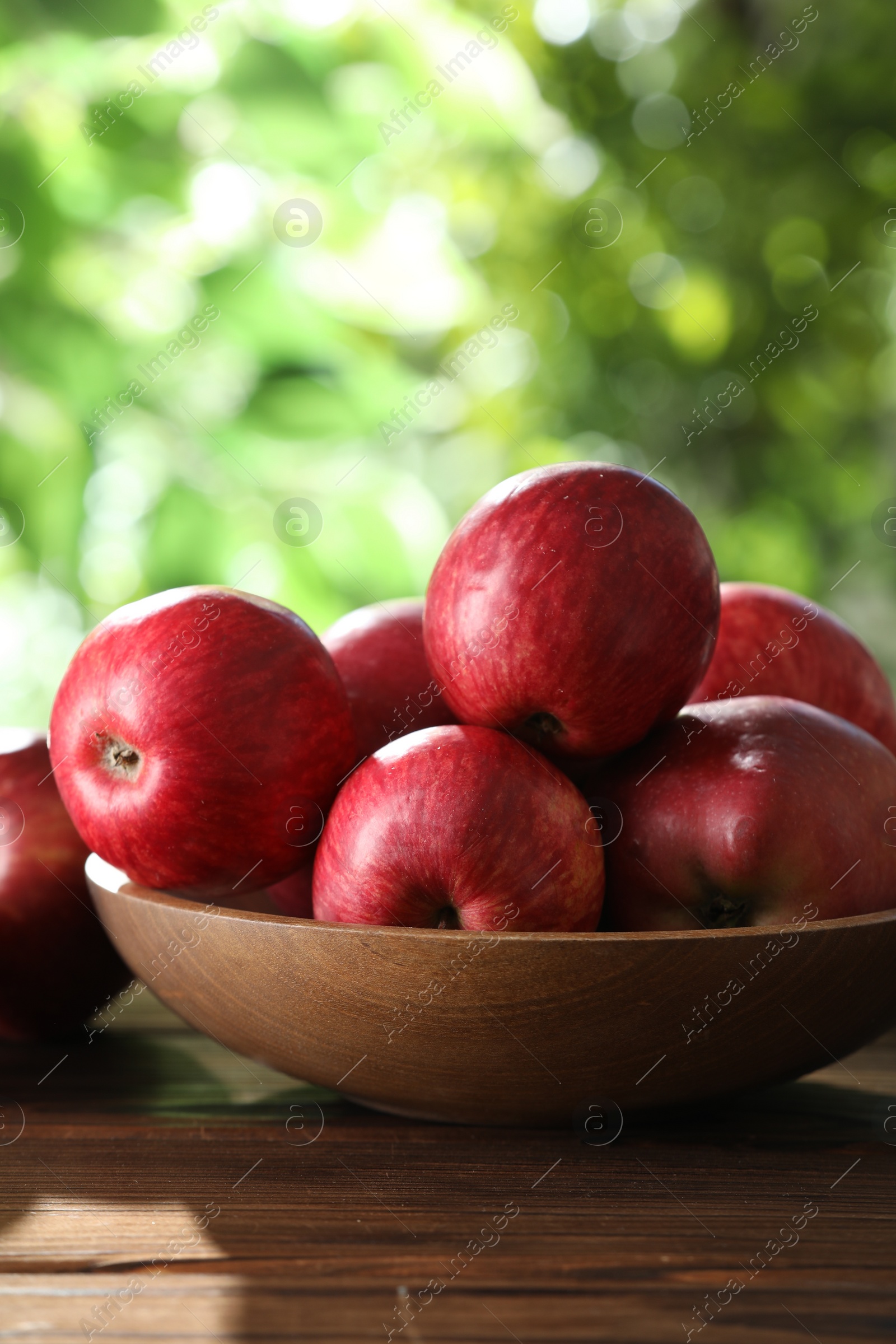 Photo of Ripe red apples in bowl on wooden table outdoors