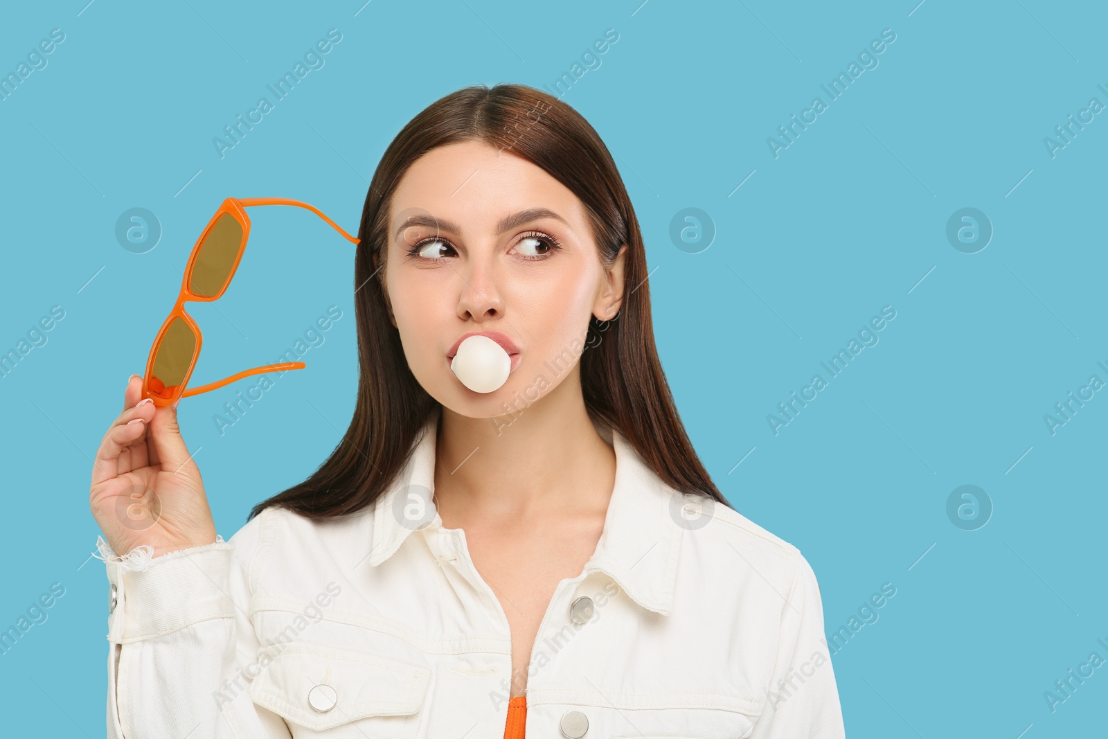 Photo of Beautiful woman with sunglasses blowing bubble gum on light blue background