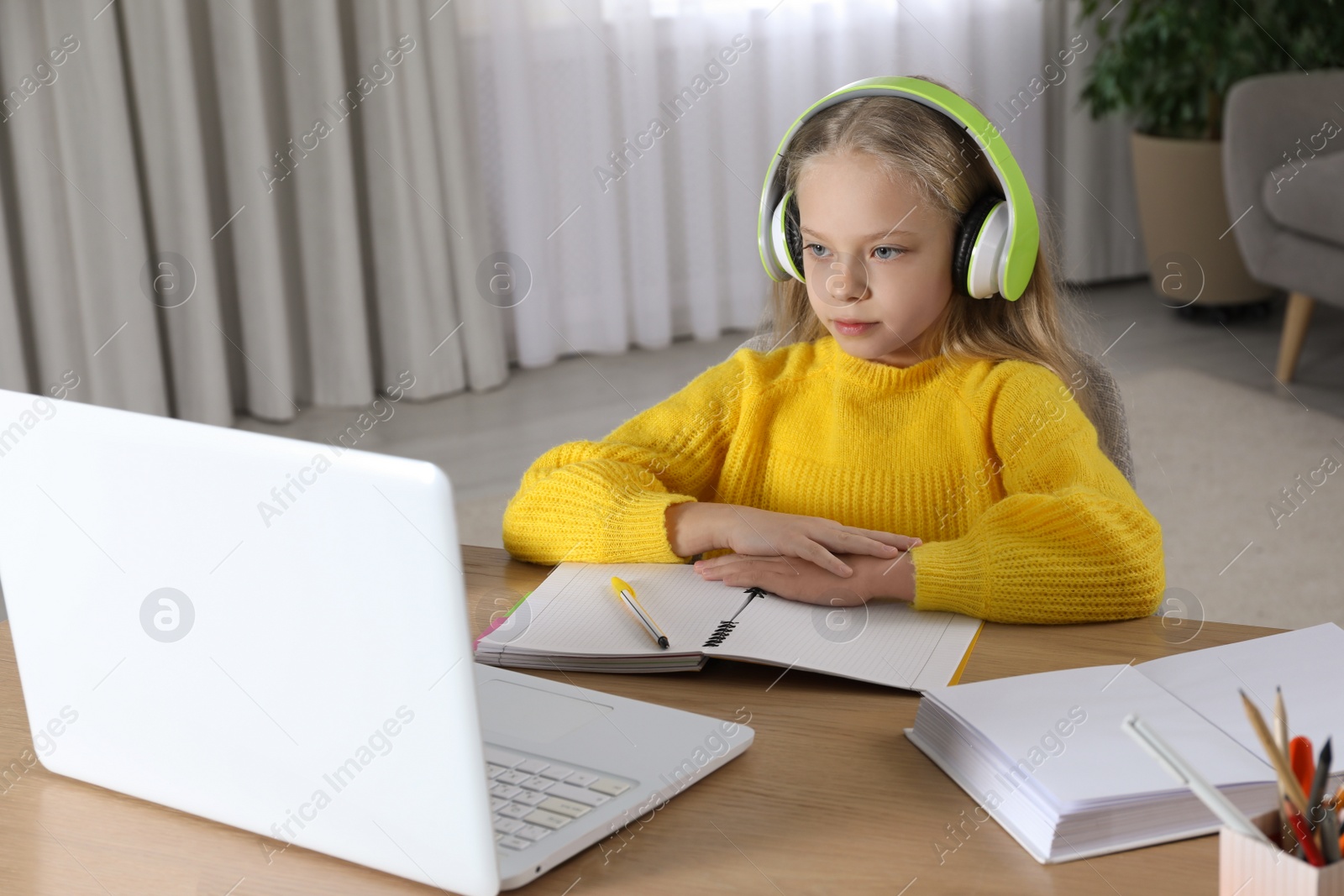 Photo of Cute little girl with modern laptop studying online at home. E-learning