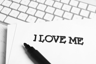 Paper with handwritten phrase I Love Me and computer keyboard on desk, closeup