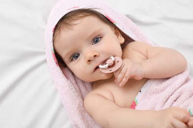 Photo of Cute little baby with pacifier in hooded towel after bathing on bed, top view