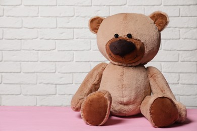 Cute teddy bear on pink wooden table near white brick wall, space for text