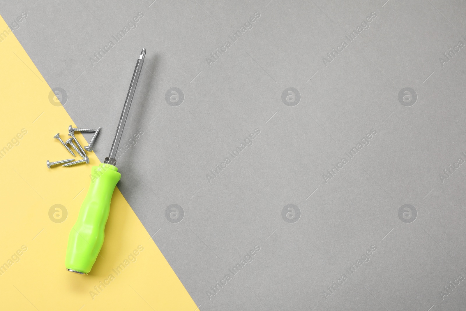 Photo of Screwdriver with green handle and screws on color background, flat lay. Space for text