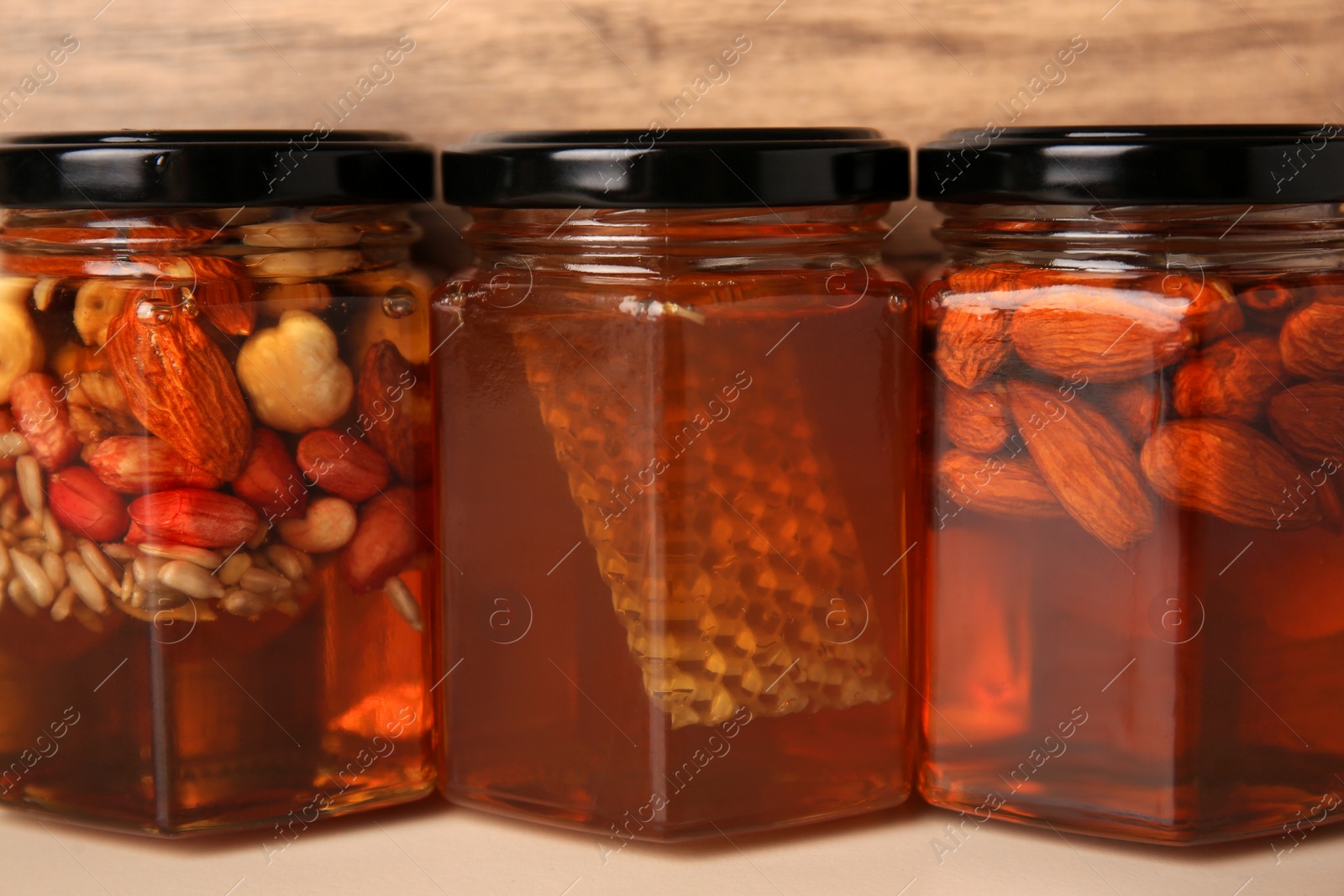 Photo of Jars with different nuts and honey on light table near wooden wall, closeup