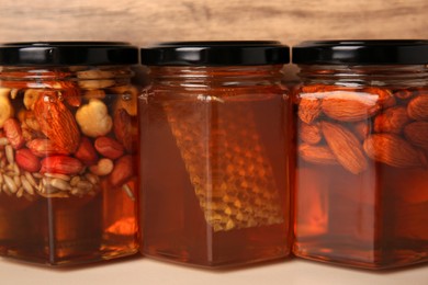 Jars with different nuts and honey on light table near wooden wall, closeup