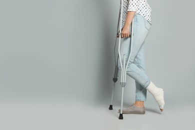 Photo of Woman with injured leg using crutches on grey background, closeup. Space for text