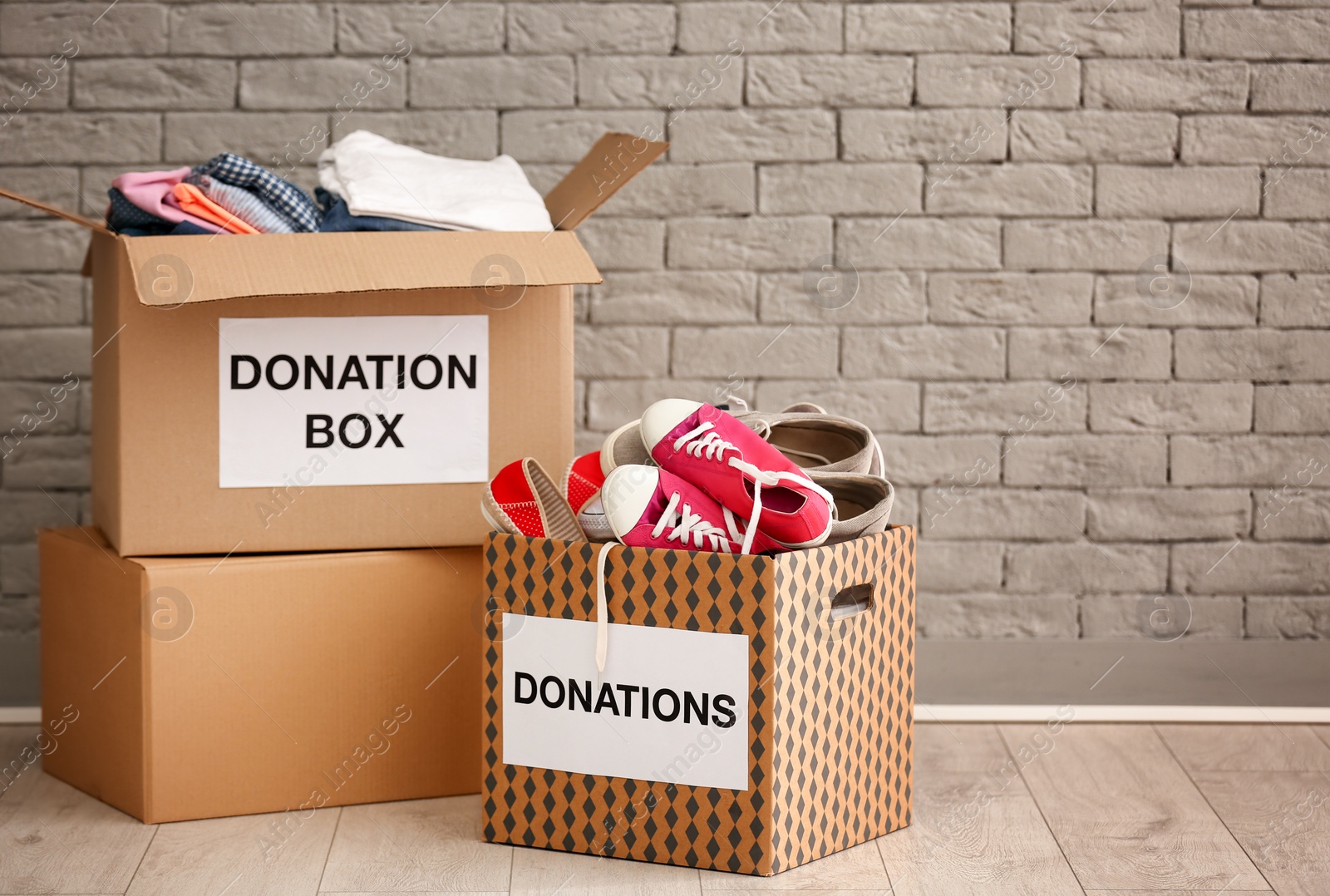 Photo of Donation boxes with clothes and shoes on floor against brick wall