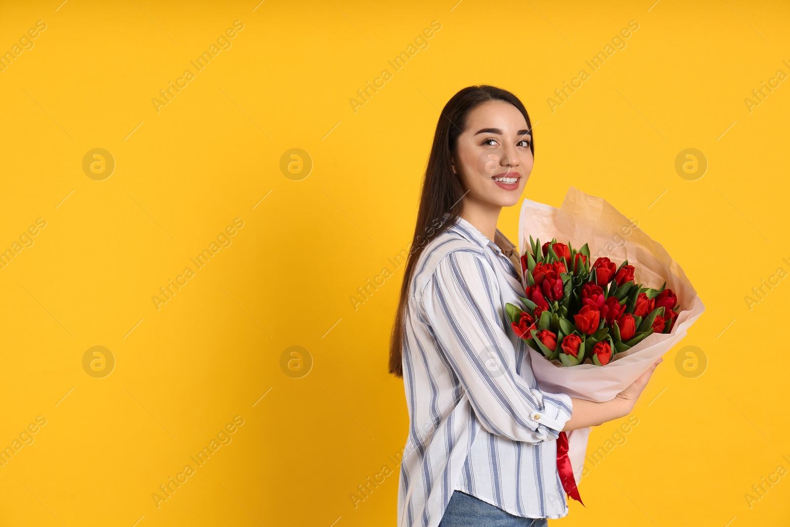 Photo of Happy woman with red tulip bouquet on yellow background, space for text. 8th of March celebration