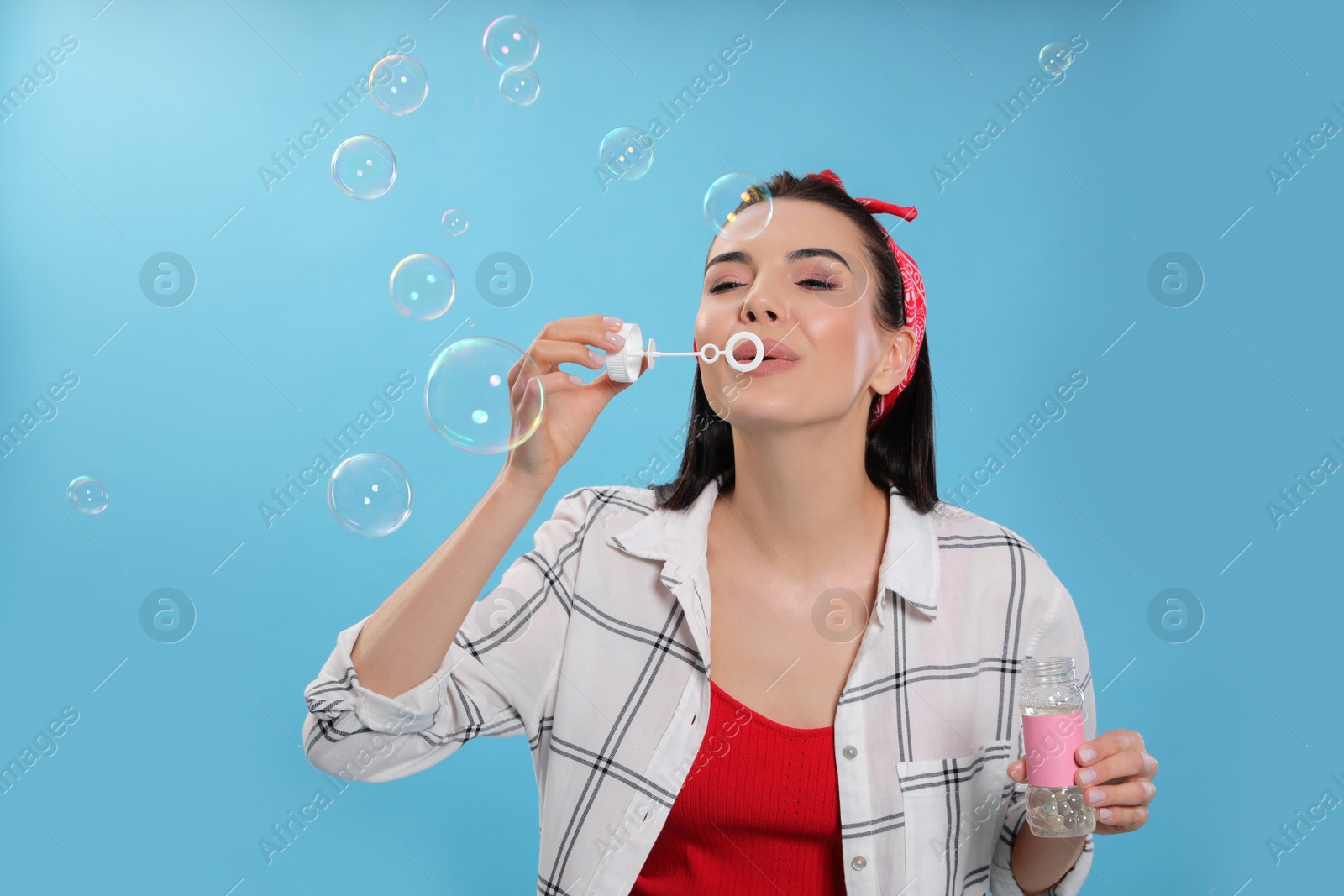 Photo of Young woman blowing soap bubbles on light blue background