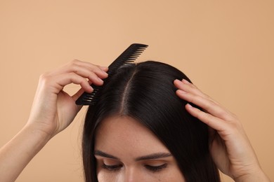 Woman with comb examining her hair and scalp on beige background, closeup