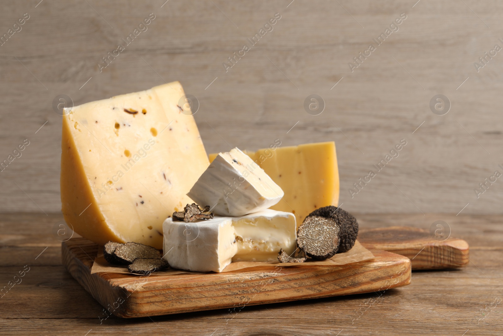 Photo of Board with delicious cheeses and fresh black truffles on wooden table