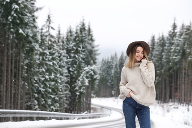 Photo of Young woman near snowy forest, space for text. Winter vacation