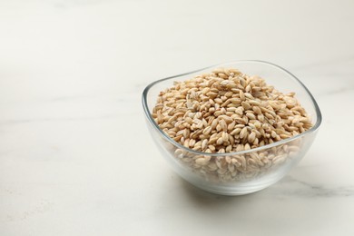 Photo of Dry pearl barley in bowl on white marble table, space for text