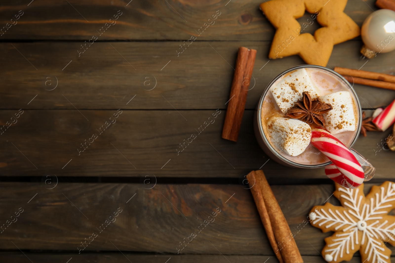 Photo of Flat lay composition with glass cup of tasty cocoa and Christmas candy cane on wooden table. Space for text